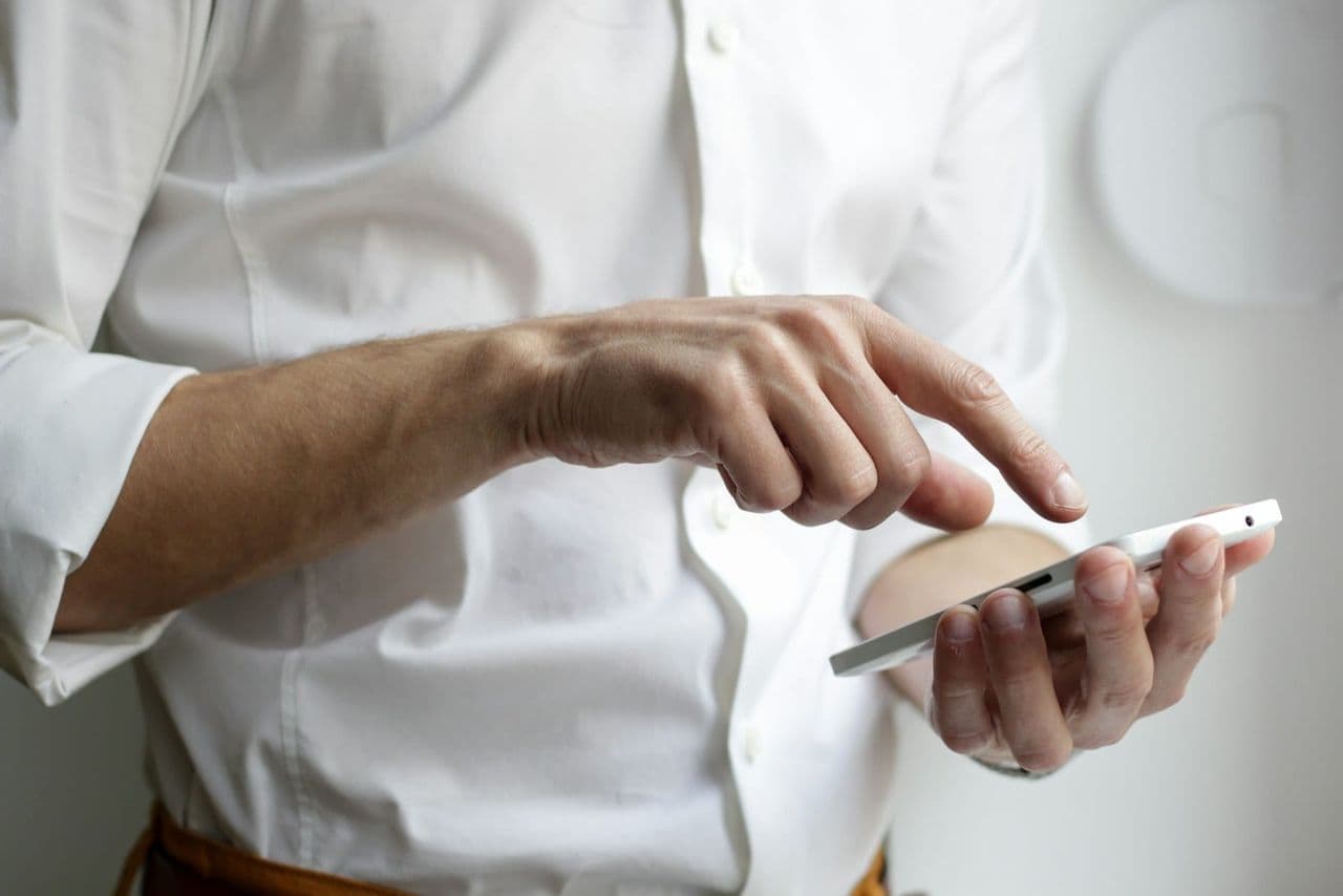 Inhaber eines kleinen Ladengeschäfts prüft auf dem Smartphone den eigenen Unternehmenseintrag in der lokalen Google-Suche