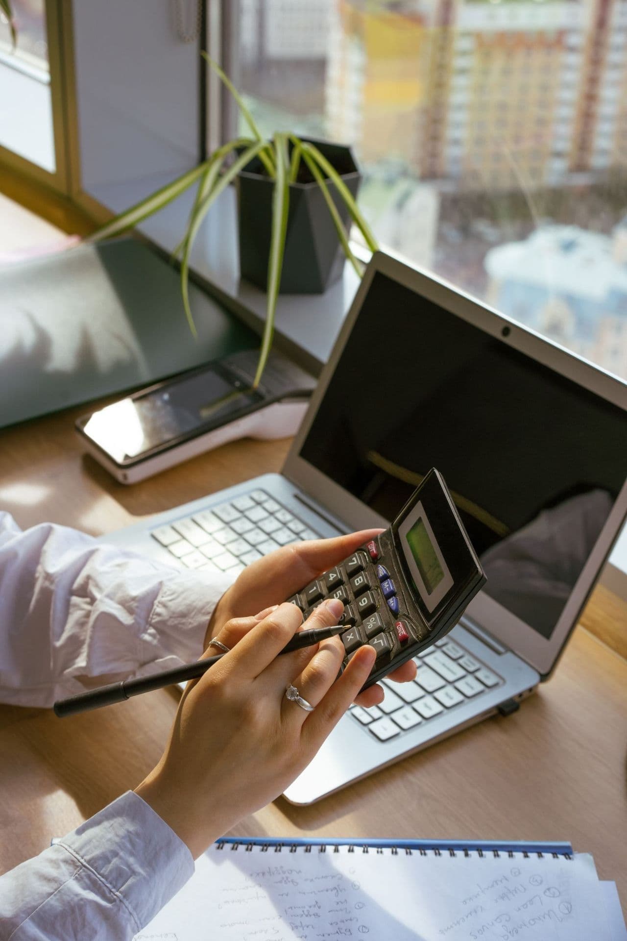 Arbeitsplatz mit Laptop, Notizblock und Taschenrechner bei der Budgetplanung für ein Website-Projekt