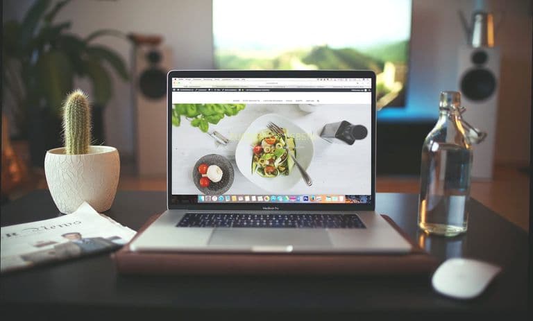 Aufgeräumter Schreibtisch mit Laptop, auf dem eine klar strukturierte Unternehmenswebsite mit deutlichem Kontakt-Button geöffnet ist