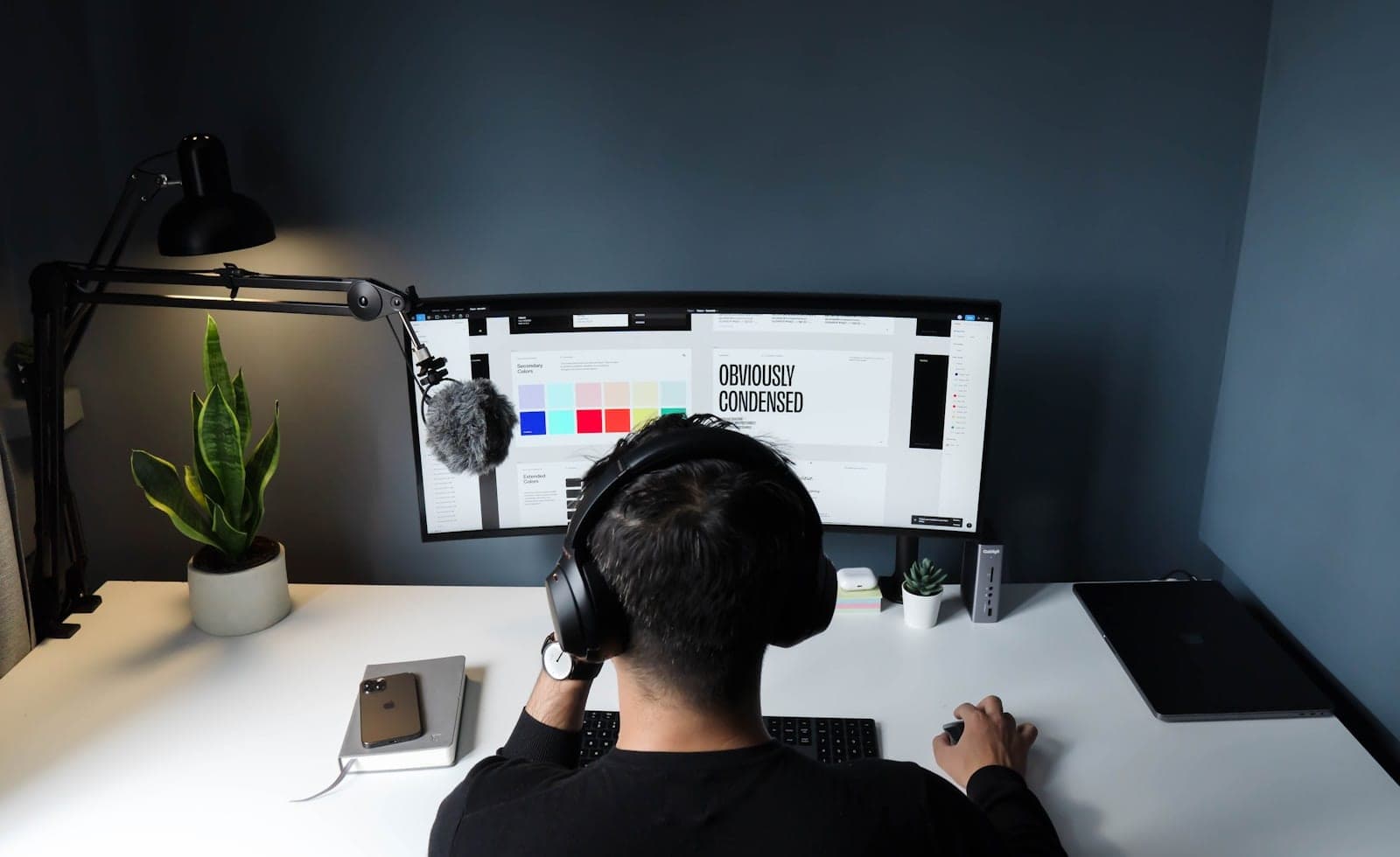Schreibtisch mit Logo-Entwicklung: Skizzen auf Papier, daneben ein Monitor mit der Vektor-Reinzeichnung eines Logos und eine abgestimmte Farbpalette als Muster